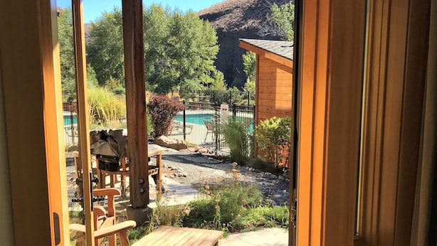 An open wooden door leading to a patio with a pool, outdoor furniture, and a view of a mountainous landscape. - The Lodge at Canyon River Ranch (Ellensburg)