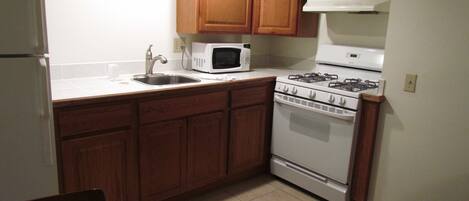 A compact kitchen with wooden cabinets, a white stove, a microwave, and a sink.