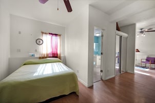 Un dormitorio con cama, ventana con cortinas, ventilador de techo y puerta que da a un baño.