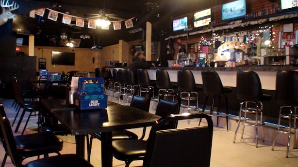 A bar area with tables and chairs, a Bud Light cooler, and a neon sign. - Schuyler Inn (Schuyler)