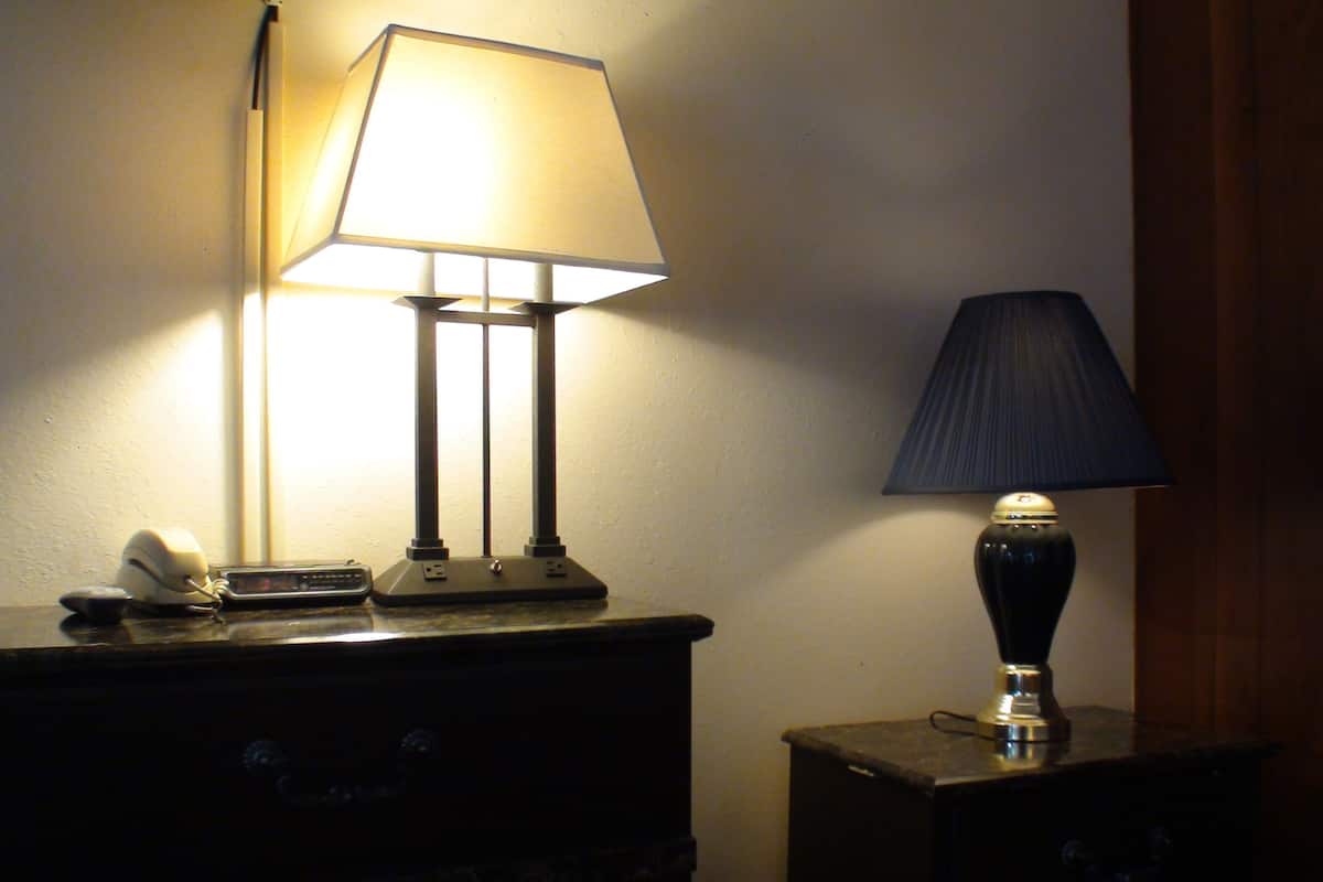 A desk with two lamps, one with a white shade and another with a dark shade, and a telephone on the left side.