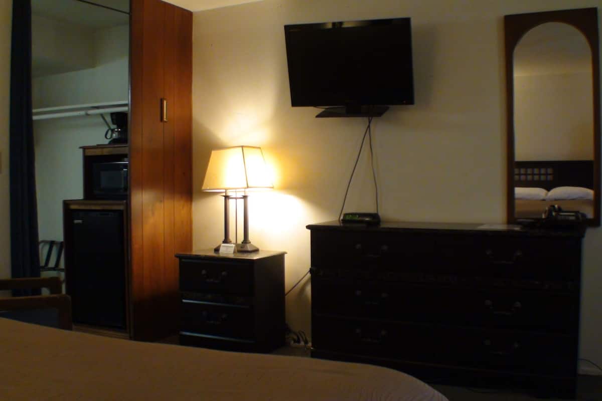 A hotel room with a bed, a dresser, a television mounted on the wall, and a mirror.