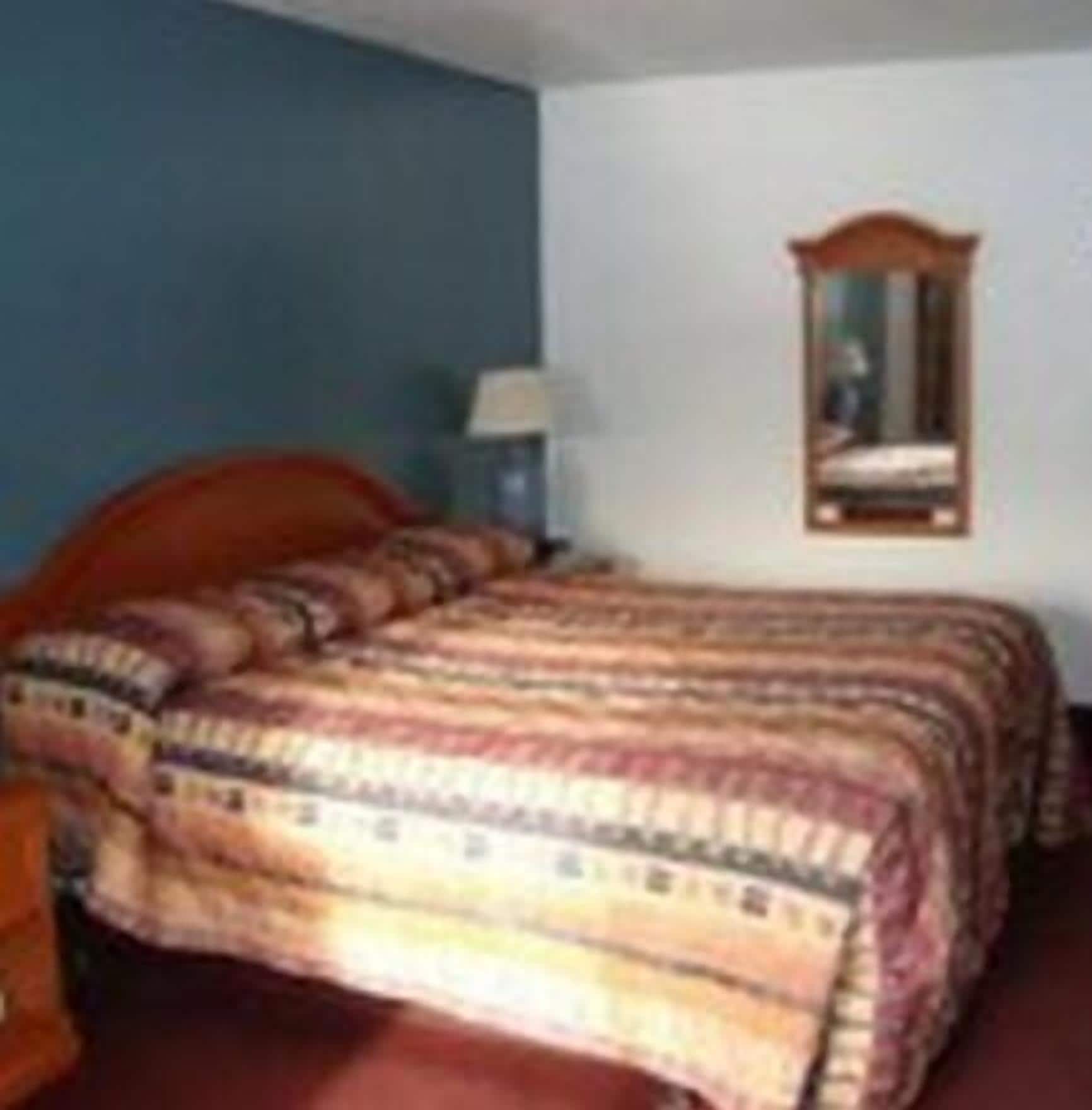 A bedroom with a bed, a nightstand, a lamp, and a mirror on the wall.