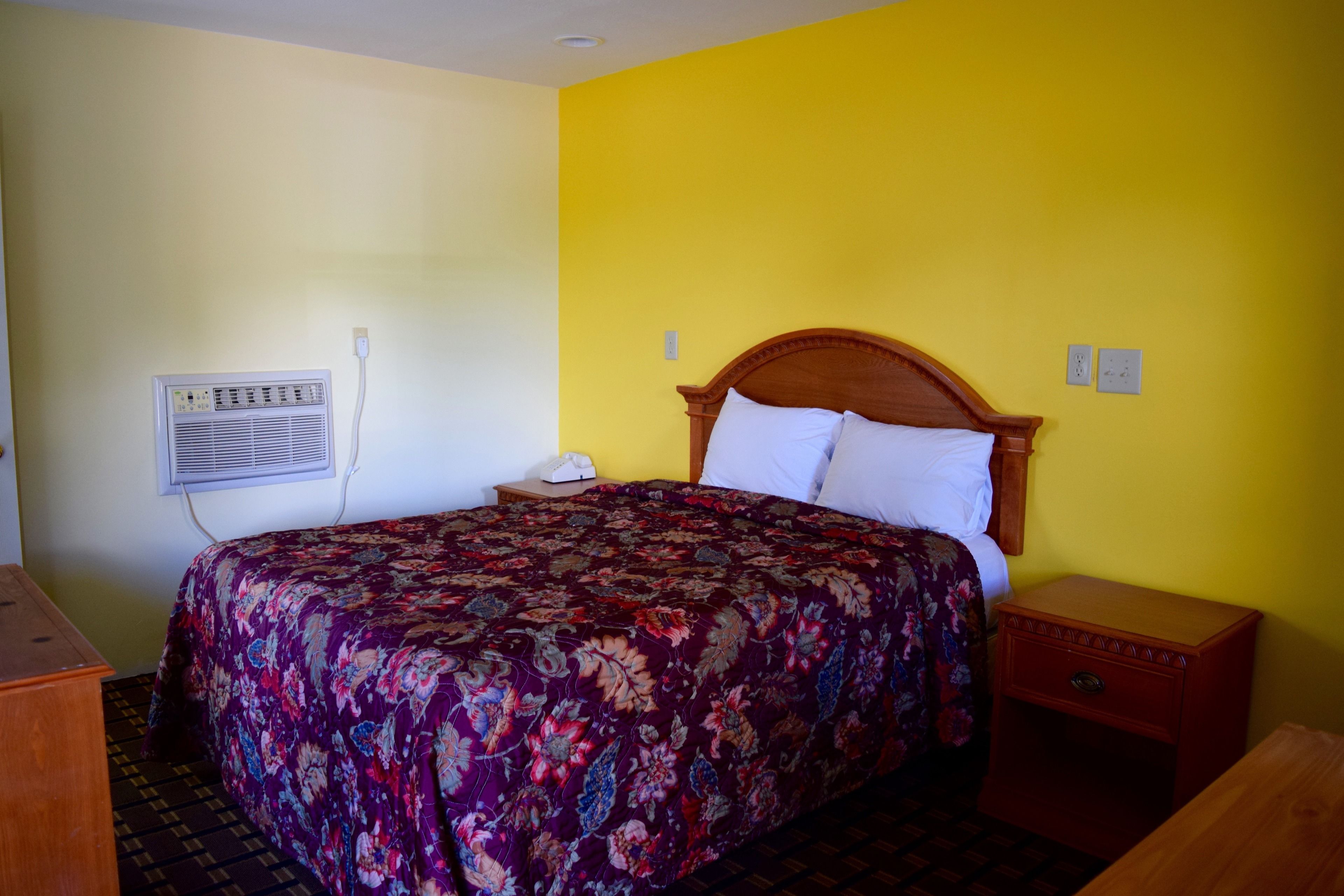 A room with a bed, a nightstand, a dresser, and a wall-mounted air conditioner.