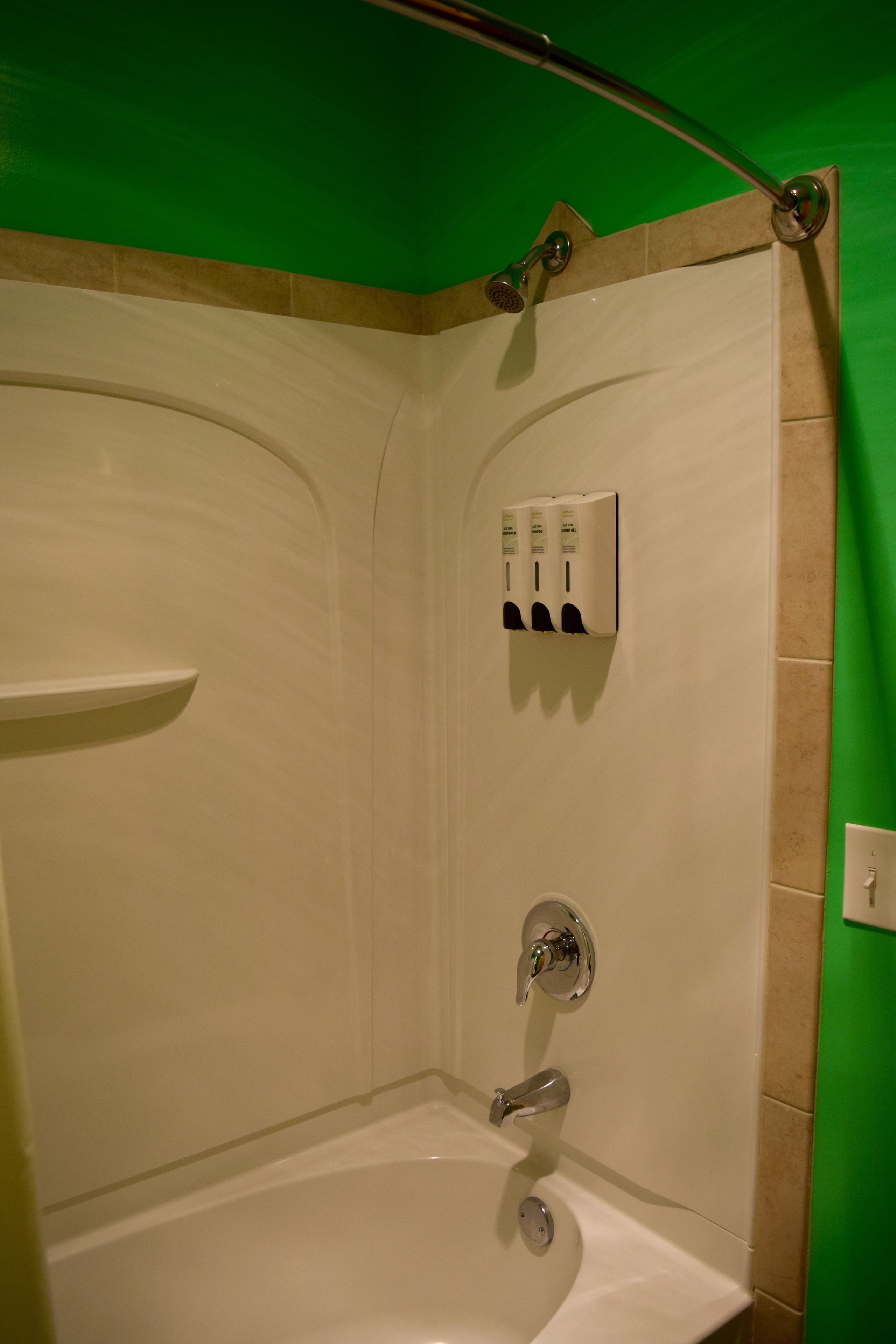 A bathroom with a bathtub, a showerhead, and a hand soap dispenser.