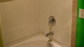 A bathroom with a bathtub, a showerhead, and a hand soap dispenser.