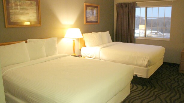 Una habitación de hotel con dos camas, una lámpara y un ventanal con cortinas.