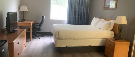A hotel room with a bed, desk, chair, TV, and a painting on the wall.