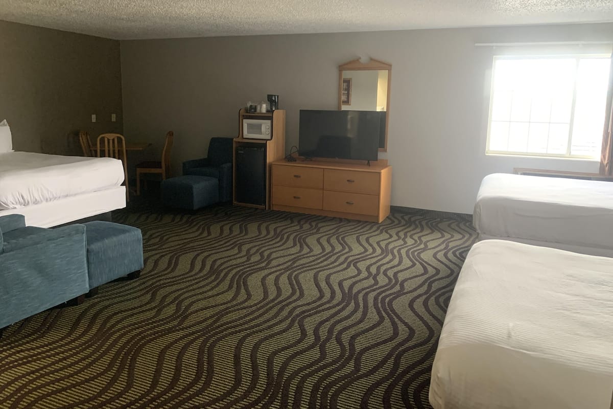A hotel room with two single beds, a desk with a television, a microwave, and a dresser.