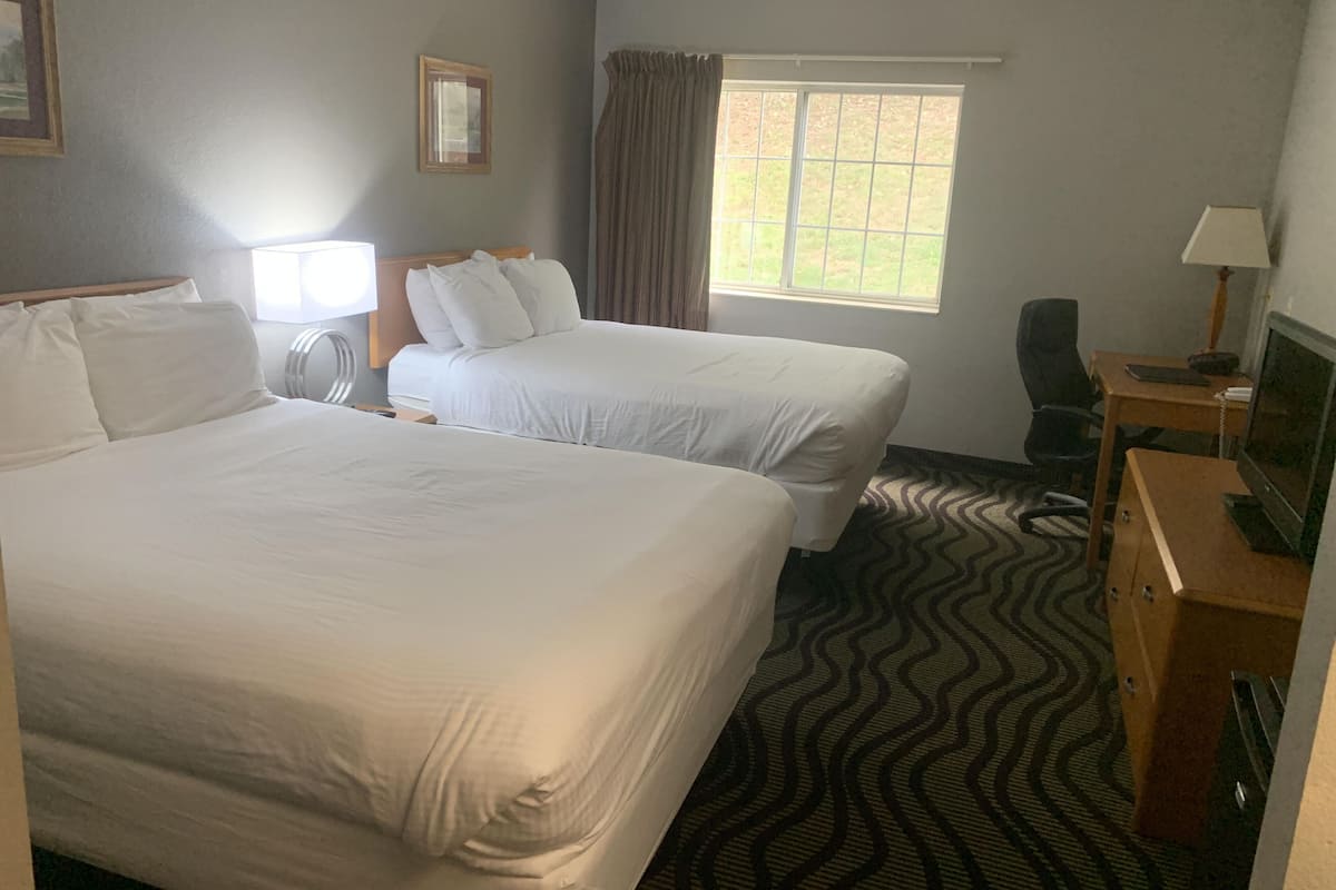 A hotel room with two beds, a desk with a computer, a television, and a window with curtains.