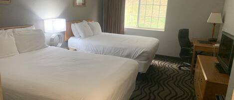 A hotel room with two beds, a desk with a computer, a television, and a window with curtains.