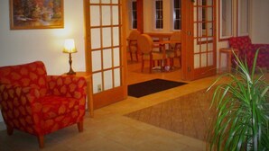 Una habitación con un sofá rojo estampado, una mesa con sillas y una puerta que da a otra estancia.