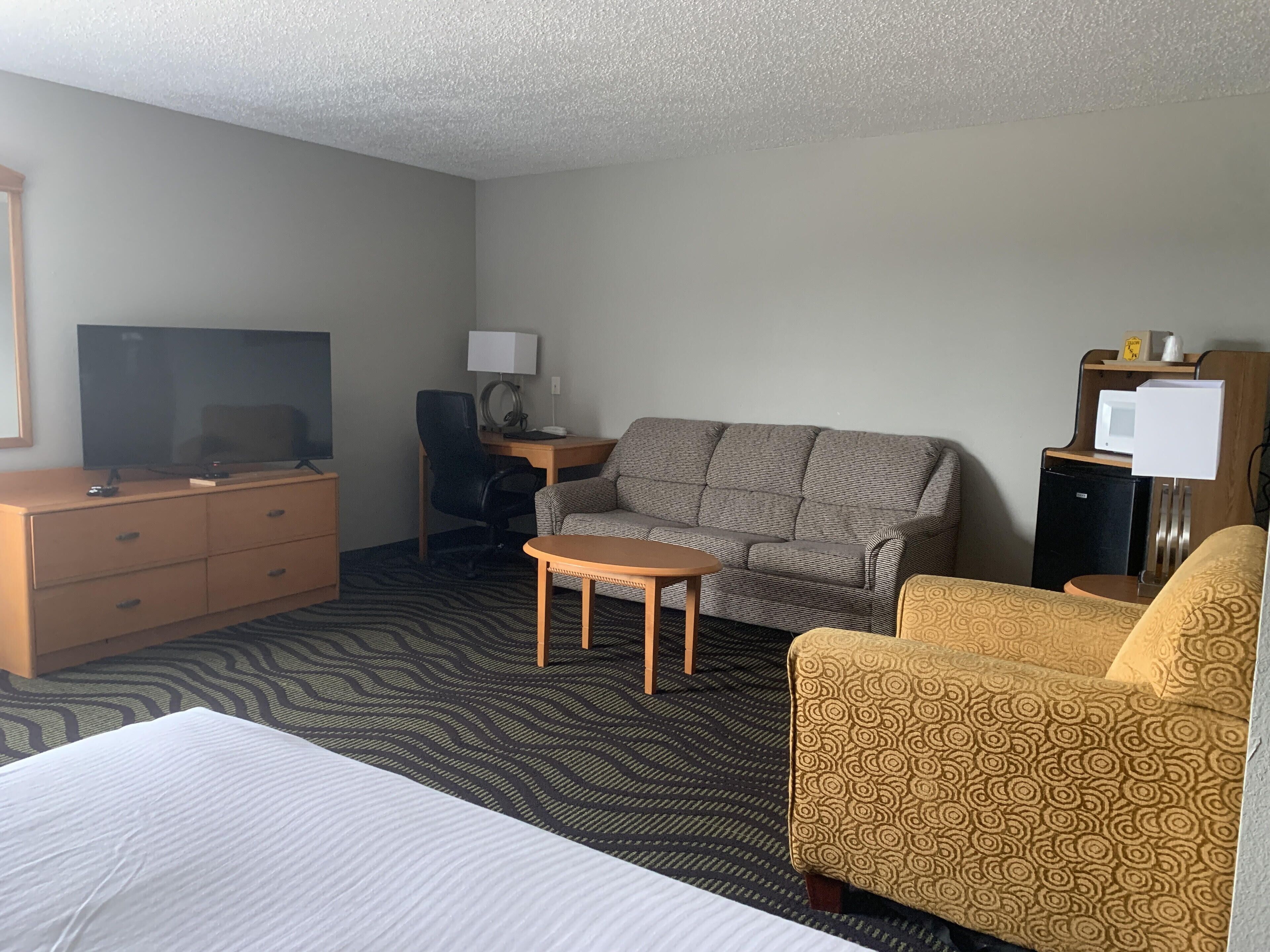 A hotel room with a bed, a sofa, a desk with a lamp, a television, and a small table.