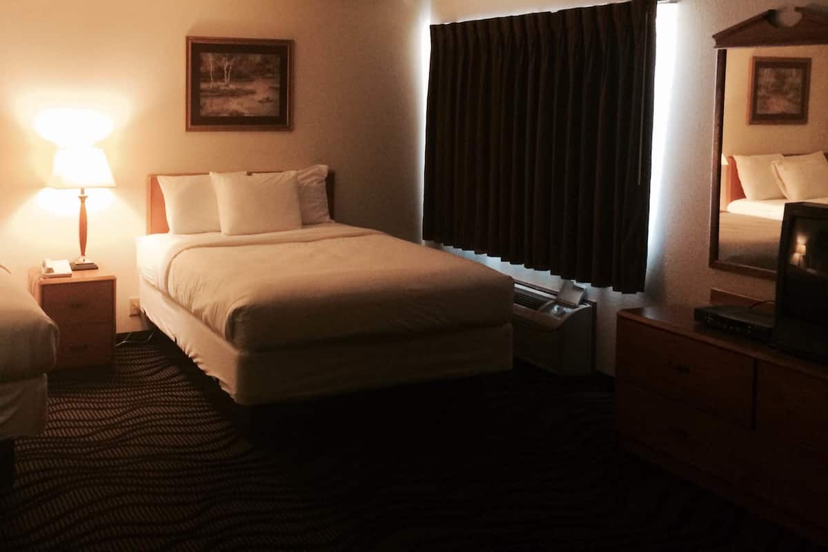 A hotel room with two beds, a nightstand with a lamp, a dresser, and a window with curtains.