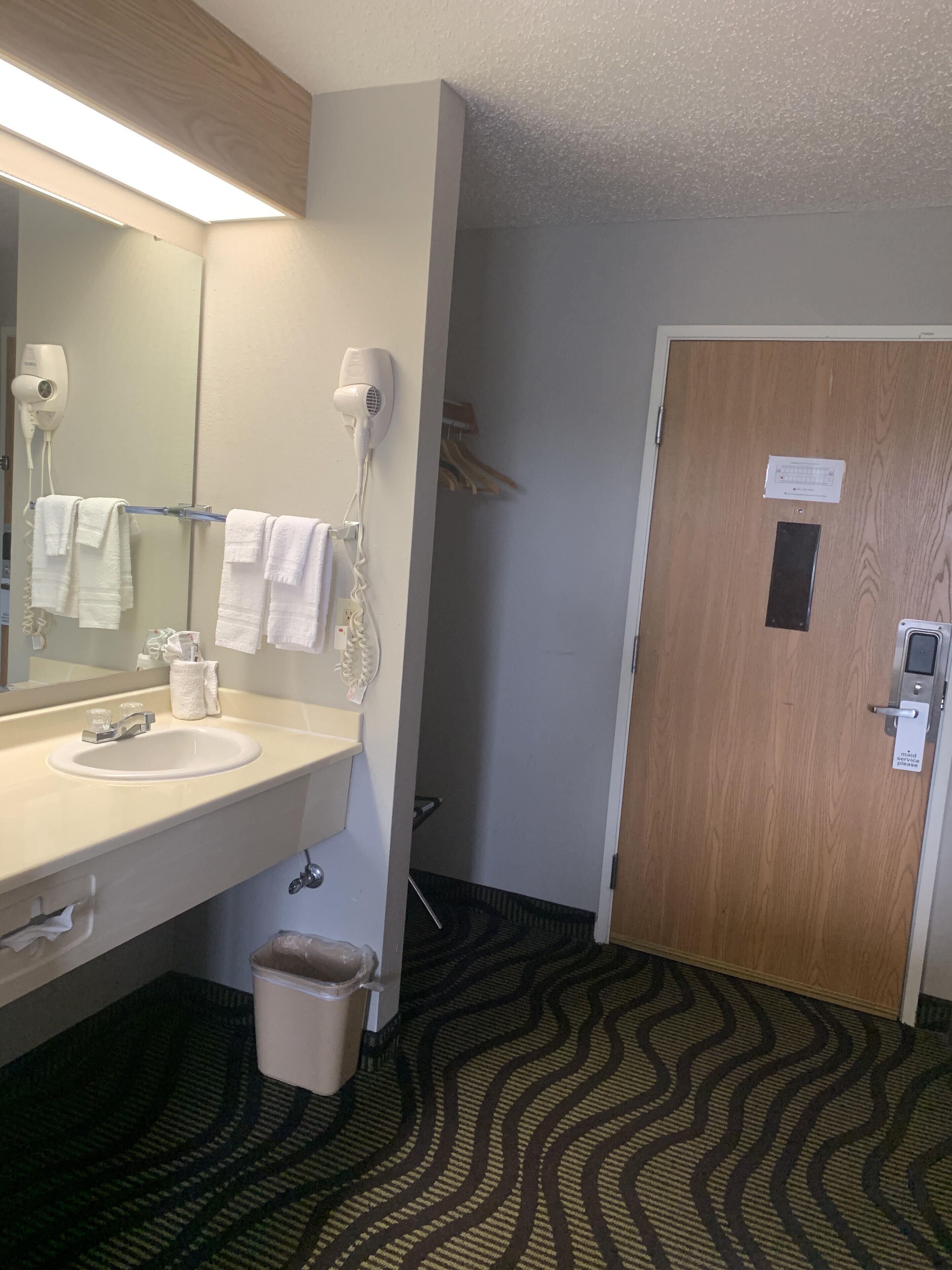 A hotel bathroom with a sink, mirror, towel rack, and a door with a service sign.