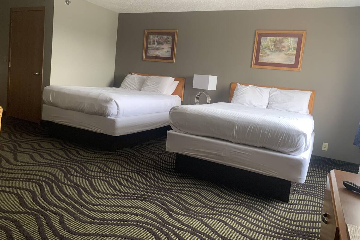 A hotel room with two beds, a patterned carpet, and two framed pictures on the wall.