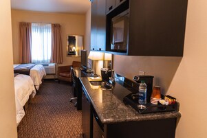 Habitación de hotel con dos camas, un escritorio con lámpara, cafetera, botella de agua y una bandeja con aperitivos.