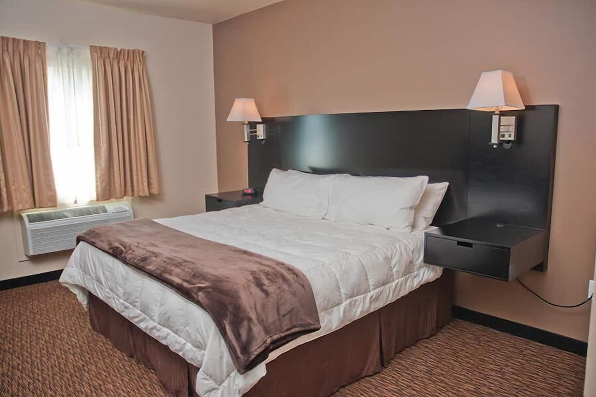 A hotel room with a large bed, two bedside tables with lamps, a wall-mounted heater, and a window with curtains.