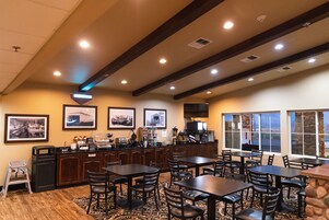 Un restaurante con mesas y sillas de madera, una barra con una máquina de café y cuadros en la pared.