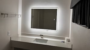 A modern bathroom with a large mirror, a white sink, and a towel rack. - Five Star Inn West Covina (West Covina)