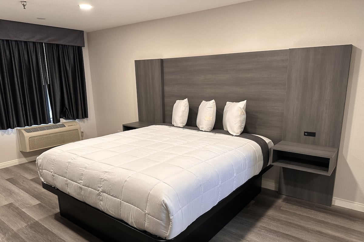 A modern bedroom with a large bed, a dark headboard, and a built-in nightstand.