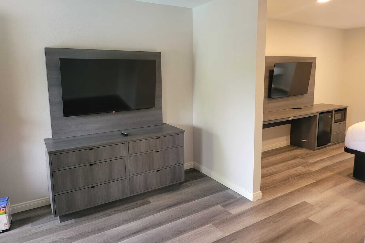 A modern room with a built-in TV and storage unit, a small kitchenette, and a wooden floor.
