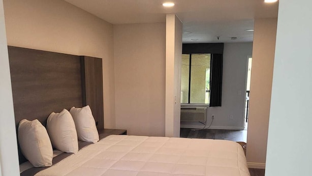 A modern bedroom with a large bed, a dark headboard, and a built-in bench at the foot of the bed. - Five Star Inn West Covina (West Covina)