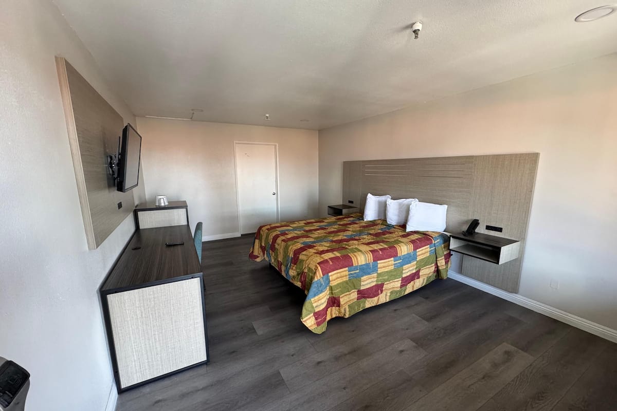 A hotel room with a bed, desk, chair, and a small table with a cup.