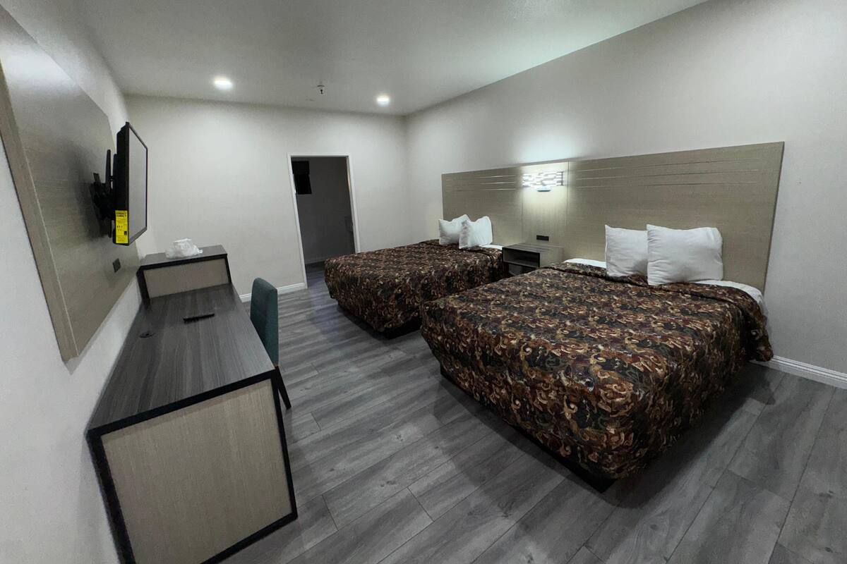 A hotel room with two beds, a desk, and a television.