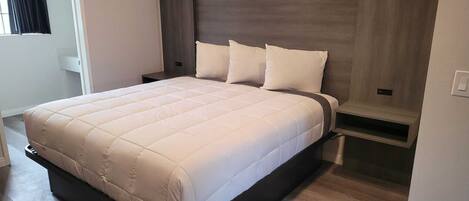 A modern bedroom with a large bed, a nightstand, a built-in bench, and a window with curtains.