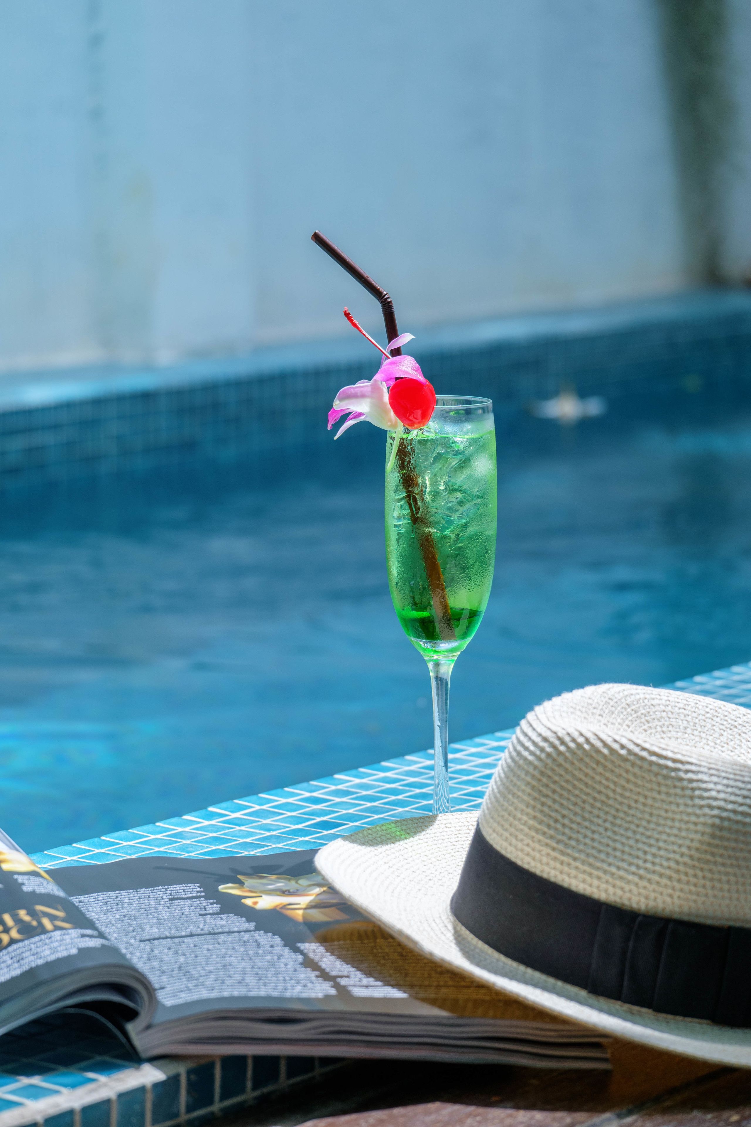 Un verre à cocktail, orné d’une cerise et d’une paille, est posé sur une table près d’une piscine.
