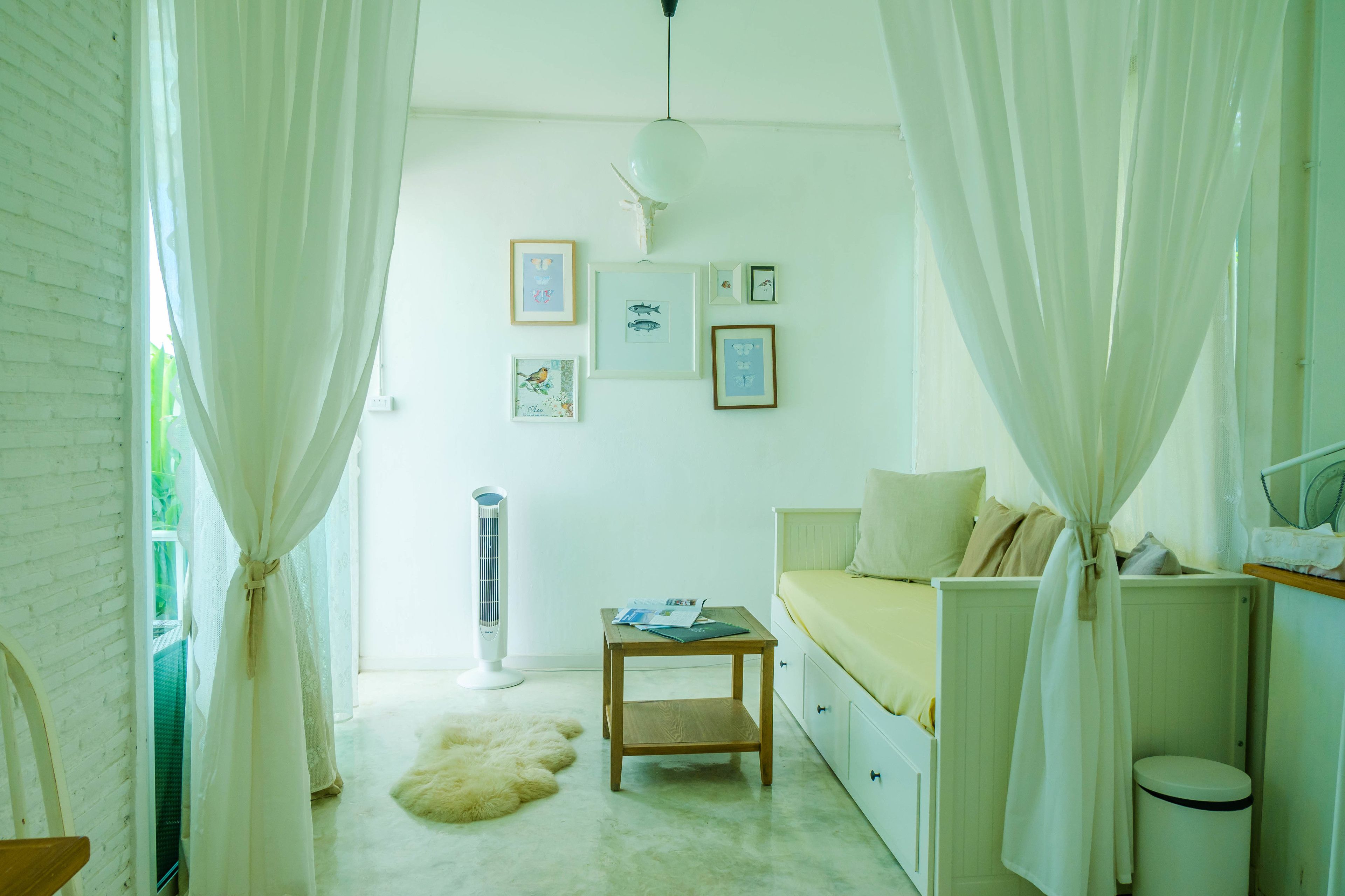 Een slaapkamer met een bed, een nachtkastje, een kleine tafel met boeken, een radiator en een muur met ingelijste foto's.