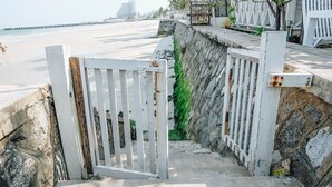 A concrete staircase leading down to a beach with a white gate at the top. - Green Gallery (Hua Hin)
