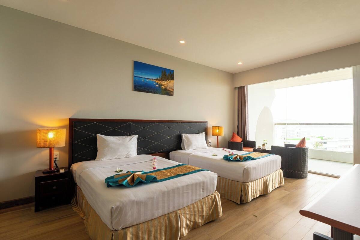 A hotel room with two beds, a dining table, and a balcony with a view.
