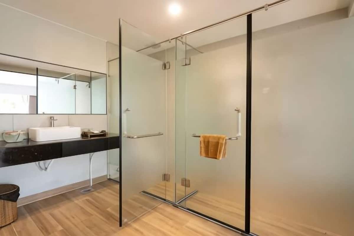 A modern bathroom with a glass shower enclosure, a large mirror, and a wooden floor.