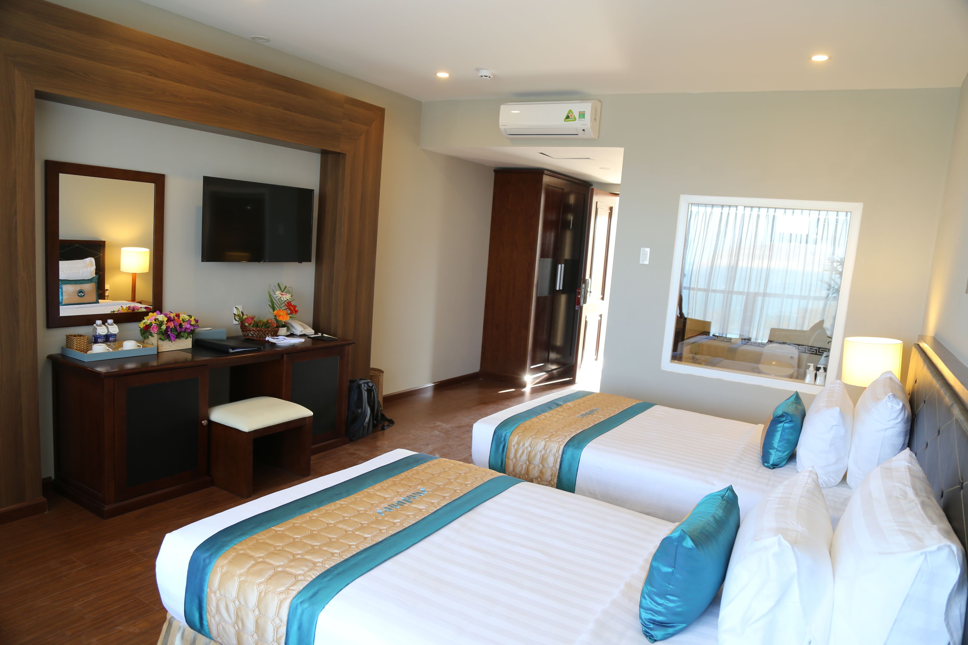A hotel room with two beds, a desk, a mirror, and a window.