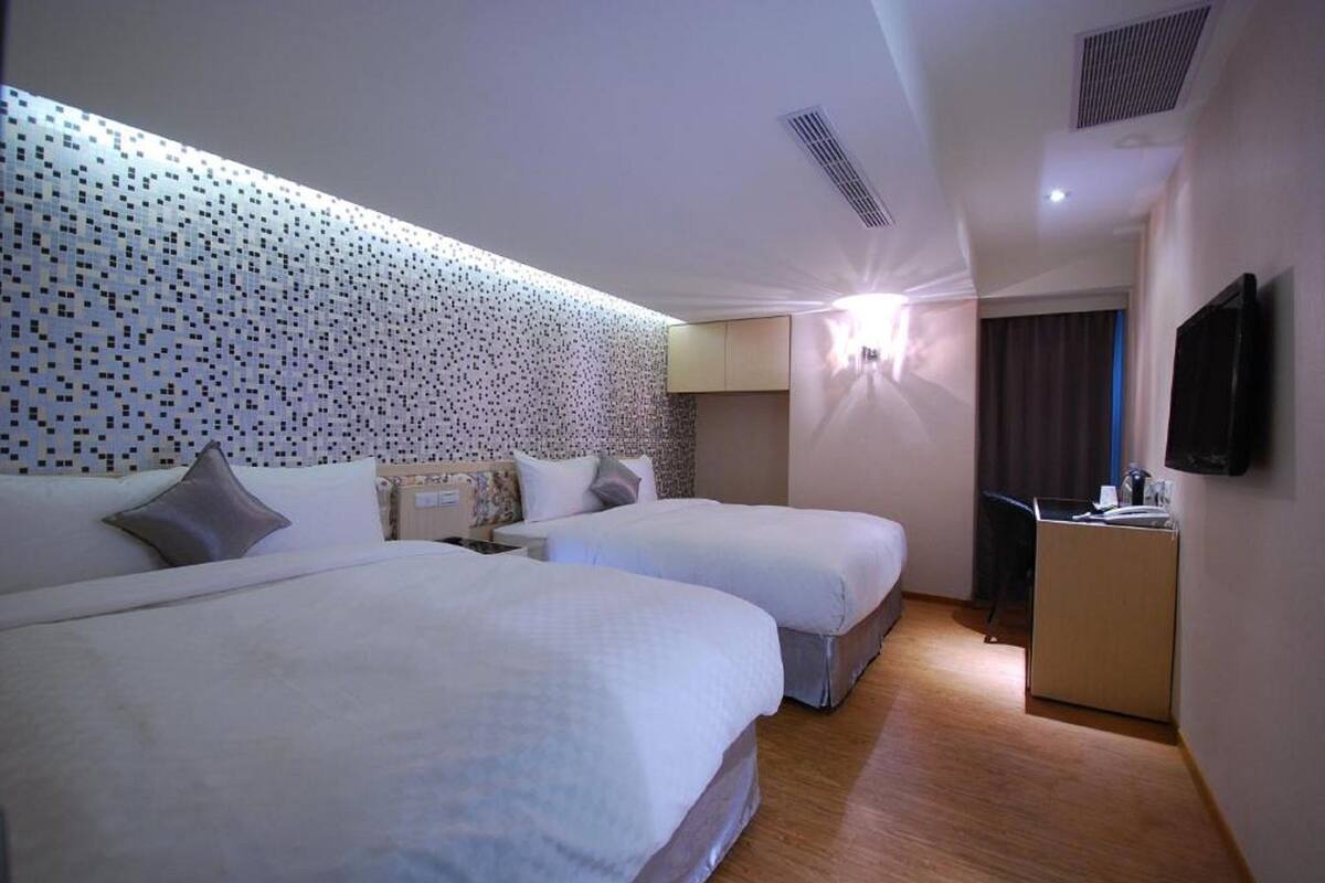 A hotel room with two beds, a desk, a television, and a patterned wall.