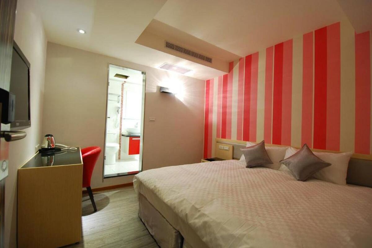 A hotel room with a bed, a desk, a chair, and a television.