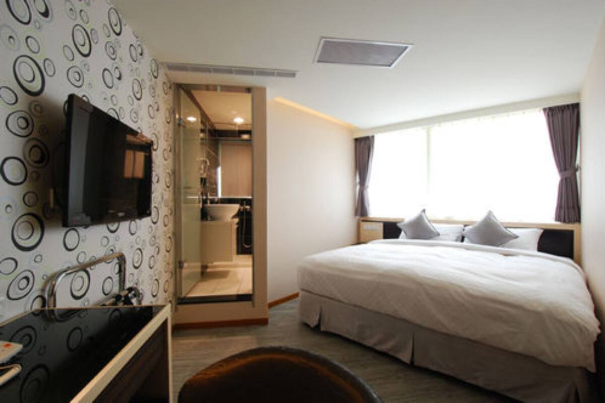 A hotel room with a bed, a TV, a bathroom, and a window with curtains.