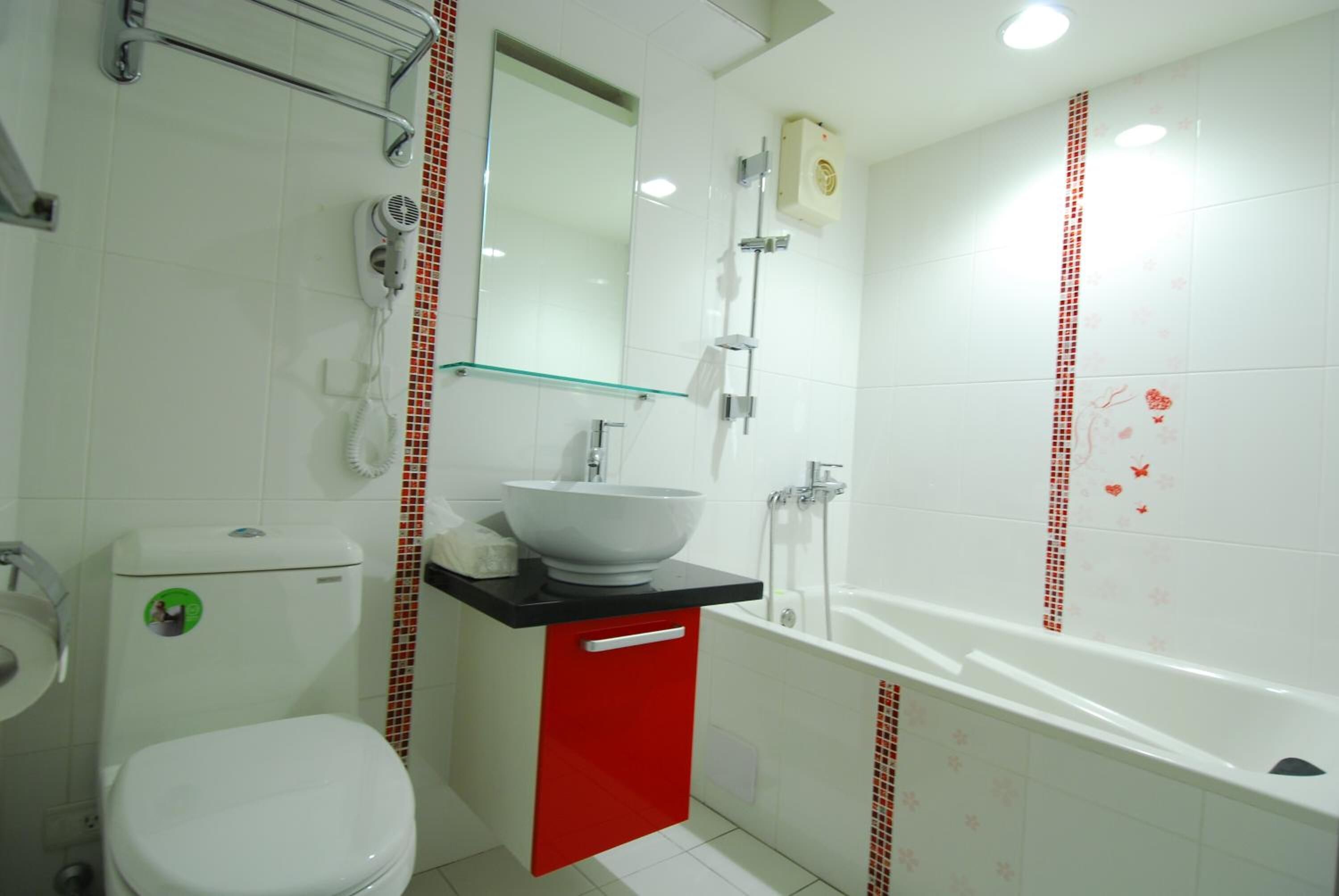 Een badkamer met een wit toilet, een rode kast, een witte wastafel en een wit bad.