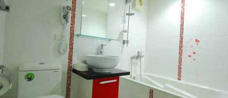 Een badkamer met een wit toilet, een rode kast, een witte wastafel en een wit bad.