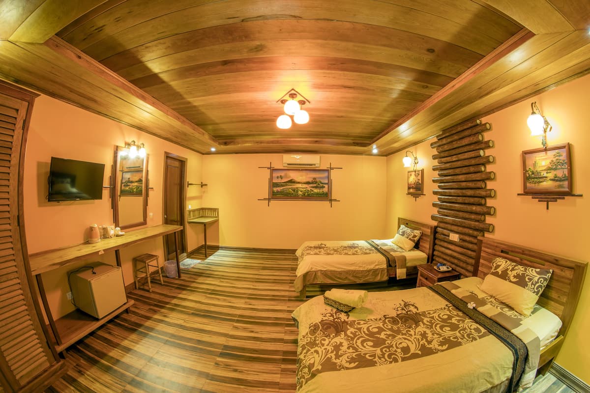 A room with two beds, a desk, and a chair. There are wall-mounted lights and a ceiling light.