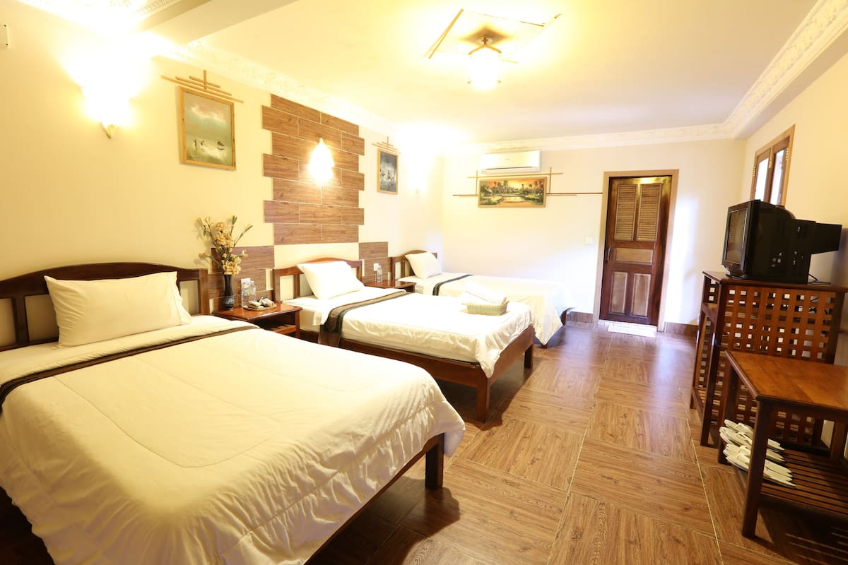 A hotel room with two beds, wooden flooring, a television, and a painting on the wall.