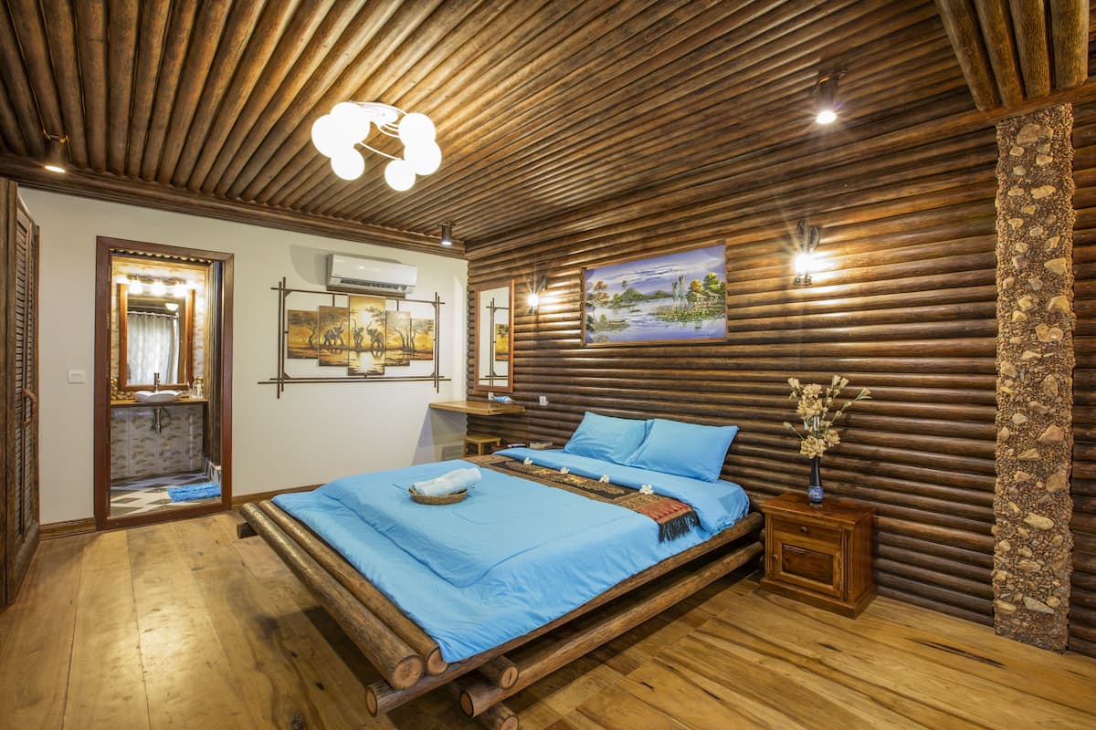A bedroom with a wooden bed frame, a blue bedspread, and a nightstand with a vase of flowers.