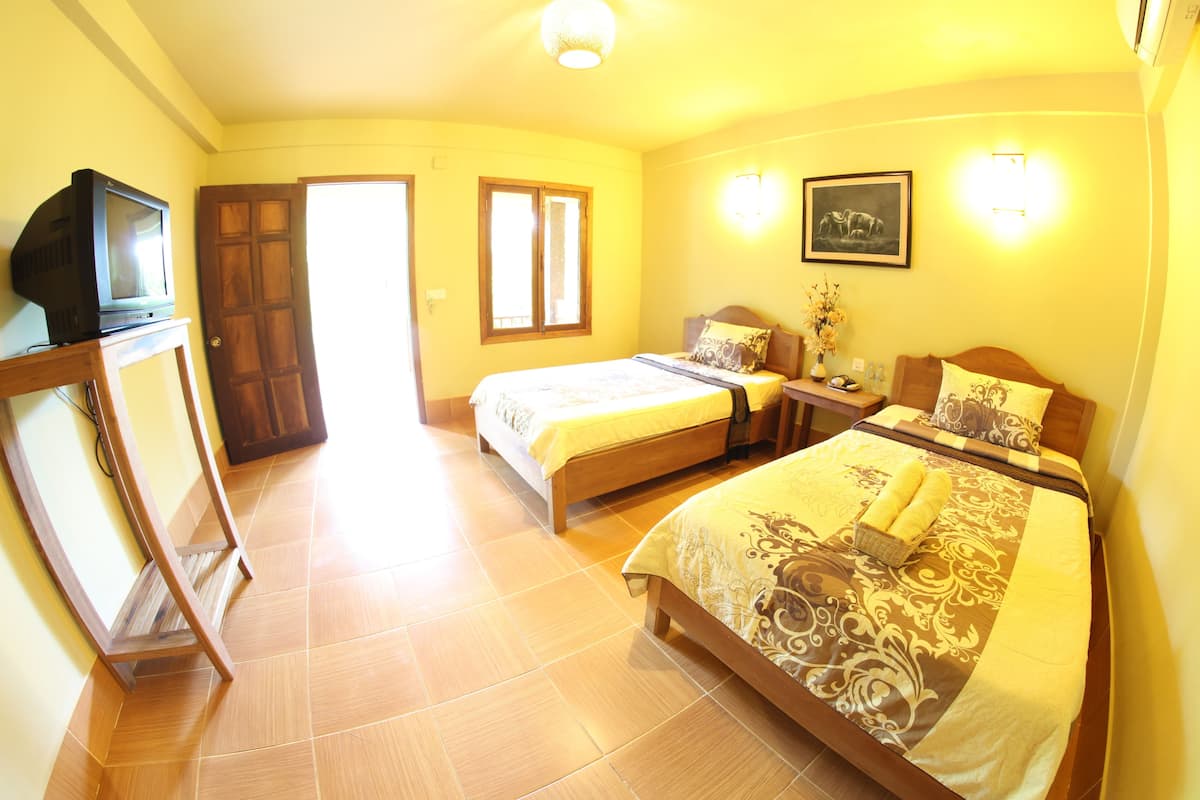 A hotel room with two beds, a TV on a stand, a bedside table with a lamp, and a picture on the wall.