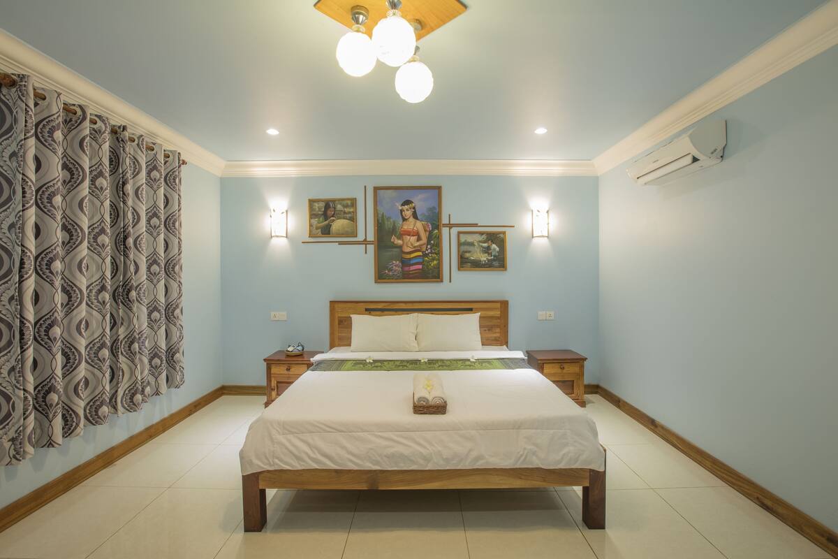 A bedroom with a wooden bed, patterned curtains, wall-mounted lights, and framed artwork.