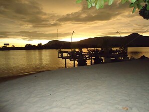 A beachside view with a wooden dock and chairs overlooking calm waters during sunset. - Natural Bungalows Restaurant and Bar (Kampot)