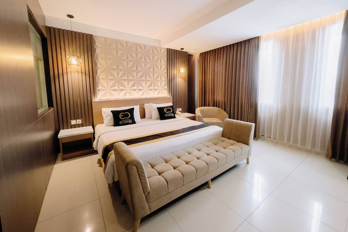 A modern hotel room with a large bed, a sofa, a nightstand, and a wall with geometric patterns.