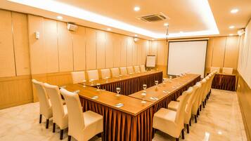 Una sala de conferencias con una larga mesa de madera, sillas blancas y una pizarra.