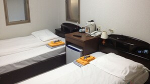 Una camera d'albergo con due letti singoli, una scrivania con telefono e lampada, una macchina per il caffè e uno specchio a parete.